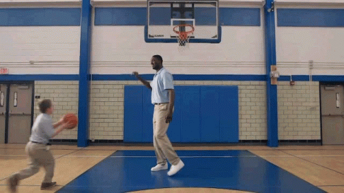 A Man And A Boy Are Playing Basketball In A Gym With An Exit Sign GIF