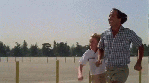 A Man And A Boy Are Running Together In A Parking Lot . GIF