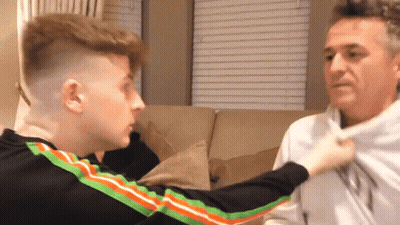 A Man And A Boy Are Sitting On A Couch And The Boy Is Holding The Man 'S Shirt . GIF