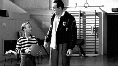 A Man And A Boy Are Standing Next To Each Other In A Gym . The Boy Is Holding A Piece Of Paper . GIF