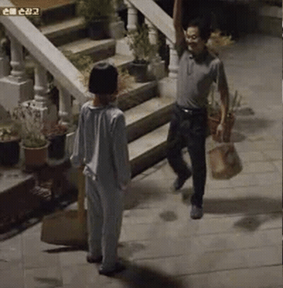 A Man And A Boy Are Standing On A Sidewalk Next To Stairs . GIF