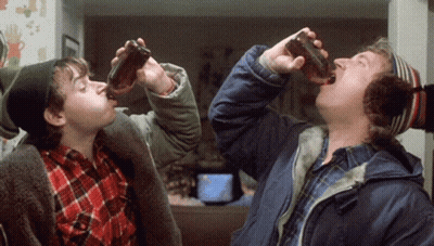 A Man And A Boy Drinking From Bottles In A Living Room GIF
