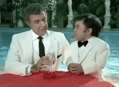A Man And A Boy In Tuxedos Are Sitting At A Table With A Glass Of Champagne . GIF