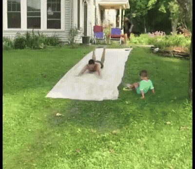 A Man And A Child Are Playing On A Water Slide . GIF