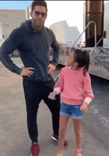 A Man And A Little Girl Are Standing Next To Each Other On A Street . GIF