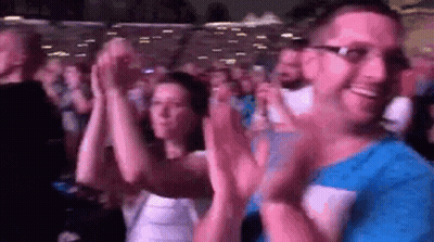 A Man And A Woman Are Clapping Their Hands In A Crowd . GIF