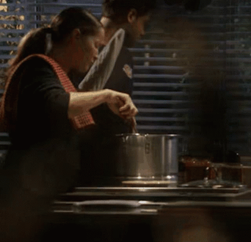 A Man And A Woman Are Cooking In A Kitchen And The Woman Has A Towel Around Her Neck GIF