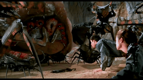A Man And A Woman Are Crawling In Front Of A Large Spider GIF