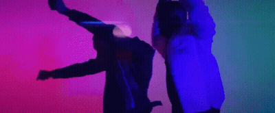 A Man And A Woman Are Dancing In A Dark Room With A Purple And Blue Light Behind Them . GIF