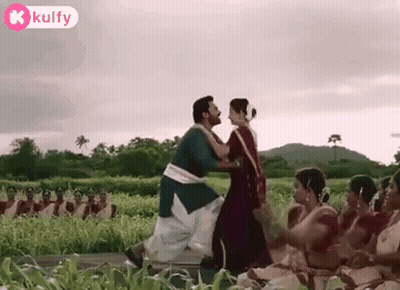 A Man And A Woman Are Dancing In A Field With A Group Of People Watching . GIF