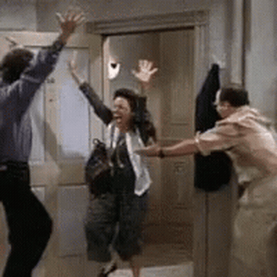 A Man And A Woman Are Dancing In A Room While A Woman Holds Her Hands Up In The Air . GIF