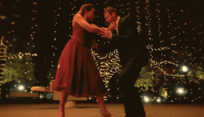 A Man And A Woman Are Dancing In Front Of A Christmas Tree GIF