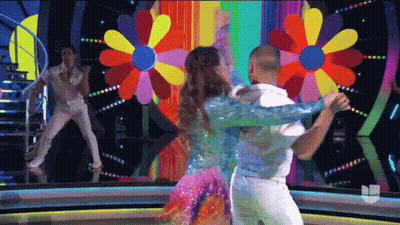 A Man And A Woman Are Dancing In Front Of A Colorful Flower Background GIF