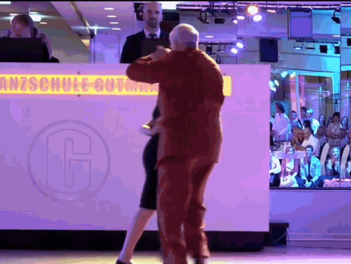 A Man And A Woman Are Dancing In Front Of A Sign That Says Anzschule GIF