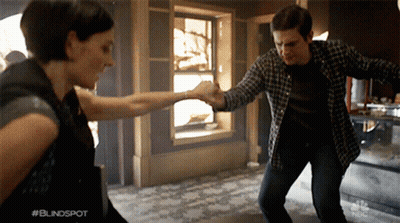 A Man And A Woman Are Dancing In Front Of A Sign That Says #Blindspot GIF
