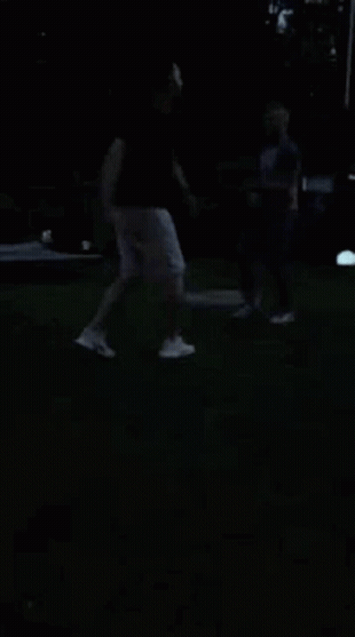 A Man And A Woman Are Dancing In The Dark On A Lush Green Field . GIF