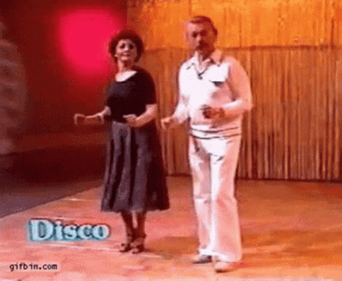 A Man And A Woman Are Dancing On A Dance Floor With A Disco Sign In The Background . GIF