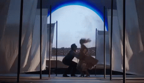 A Man And A Woman Are Dancing On A Stage In Front Of A Large Window . GIF