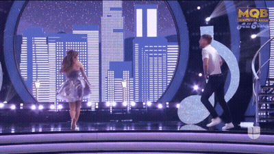 A Man And A Woman Are Dancing On A Stage With Mqbe On The Bottom Right GIF