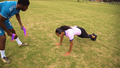 A Man And A Woman Are Doing Push Ups On A Grassy Field GIF