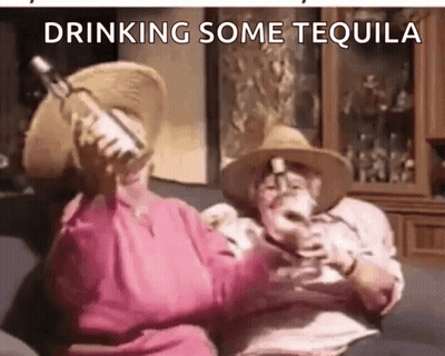 A Man And A Woman Are Drinking Tequila On A Couch . GIF
