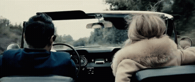A Man And A Woman Are Driving In A Car With The Woman Wearing A Fur Coat GIF