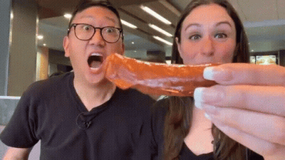A Man And A Woman Are Eating A Sausage Together . GIF