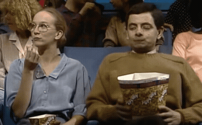 A Man And A Woman Are Eating Popcorn In A Theater . GIF