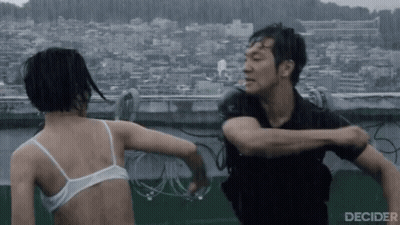 A Man And A Woman Are Fighting In The Rain . The Woman Is Wearing A White Bra . GIF