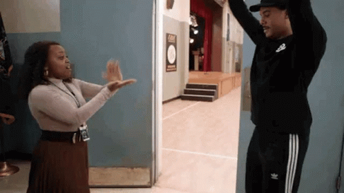 A Man And A Woman Are Giving Each Other A High Five In A Doorway . GIF