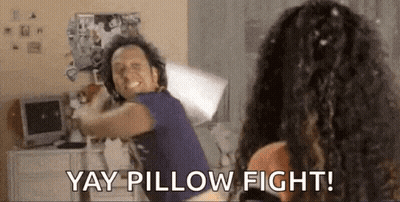 A Man And A Woman Are Having A Pillow Fight In A Room . GIF