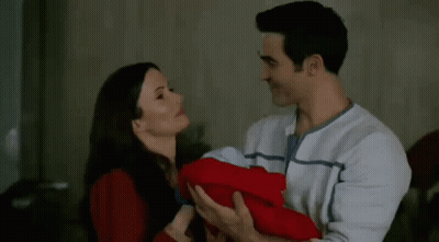 A Man And A Woman Are Holding A Baby And Kissing . GIF