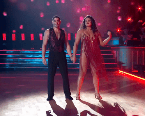 A Man And A Woman Are Holding Hands While Dancing On A Stage GIF