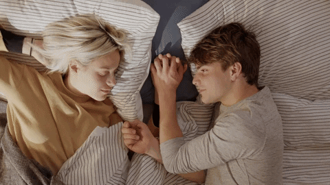 A Man And A Woman Are Holding Hands While Laying In Bed GIF