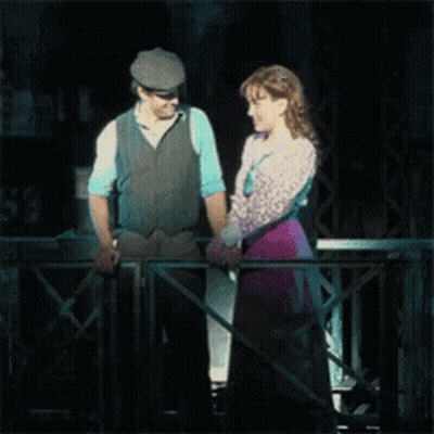 A Man And A Woman Are Holding Hands While Standing On A Balcony GIF
