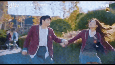 A Man And A Woman Are Holding Hands While Walking Down A Sidewalk . GIF