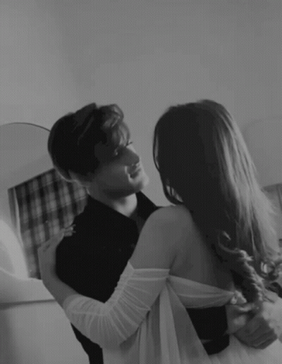 A Man And A Woman Are Hugging And Looking At Each Other In A Black And White Photo . GIF
