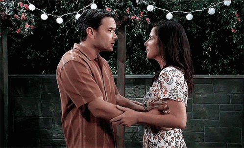 A Man And A Woman Are Hugging And Looking At Each Other In Front Of A Brick Wall GIF