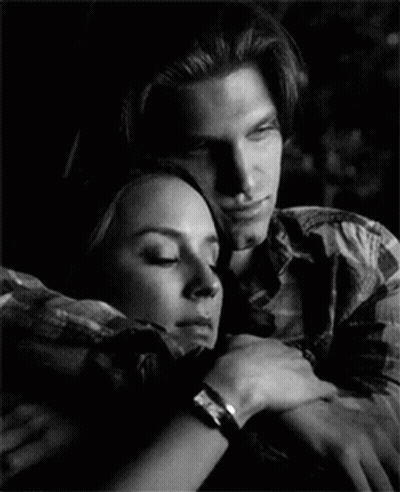 A Man And A Woman Are Hugging Each Other In A Black And White Photo GIF