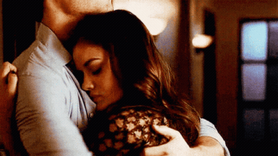 A Man And A Woman Are Hugging Each Other In A Hallway . GIF