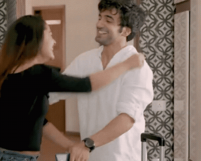 A Man And A Woman Are Hugging Each Other In A Room With A Patterned Wall . GIF