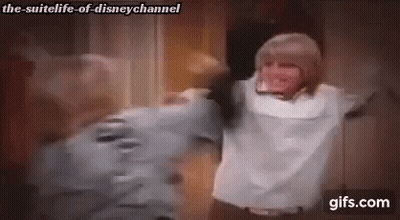 A Man And A Woman Are Hugging Each Other In A Room With Their Arms Outstretched . GIF
