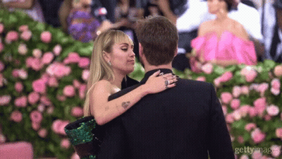 A Man And A Woman Are Hugging Each Other In Front Of Flowers GIF
