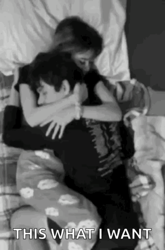 A Man And A Woman Are Hugging Each Other On A Bed In A Black And White Photo . GIF