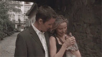 A Man And A Woman Are Hugging Each Other While Standing Next To A Stone Wall . GIF