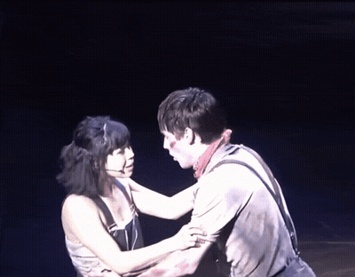 A Man And A Woman Are Hugging On A Stage In The Dark GIF