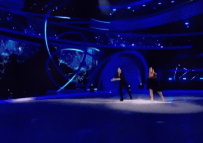 A Man And A Woman Are Ice Skating On A Stage GIF