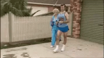 A Man And A Woman Are Jogging Down A Sidewalk . GIF