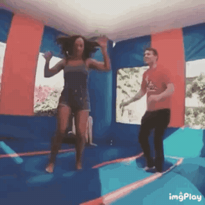 A Man And A Woman Are Jumping In A Bouncy House GIF