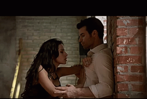 A Man And A Woman Are Kissing Against A Brick Wall . GIF